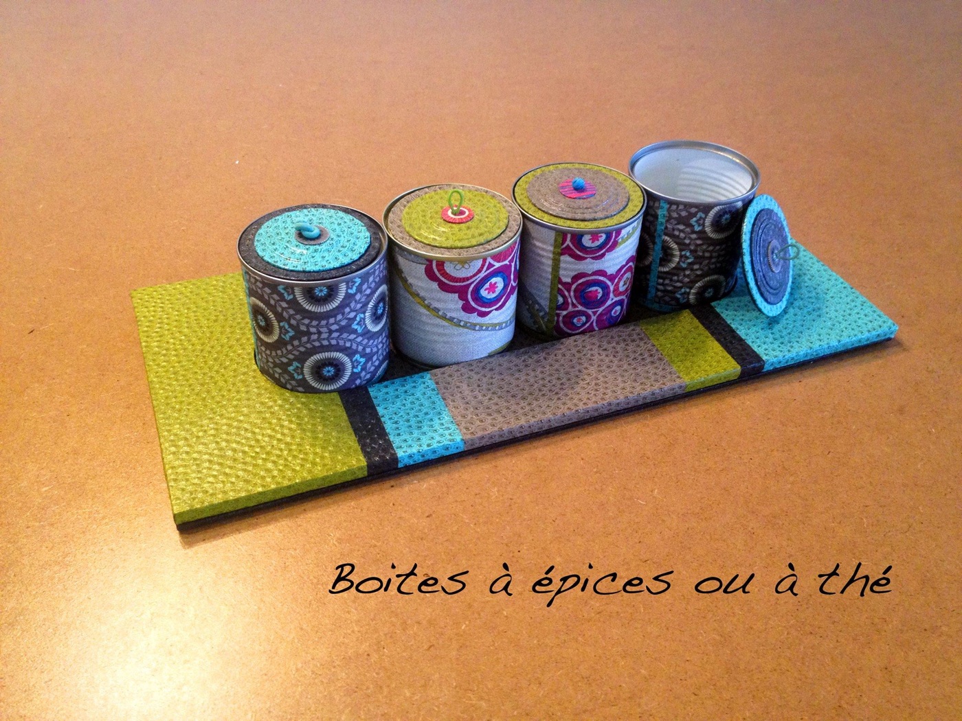 Quatre boîtes à épices habillées de papiers à motifs sur leur plateau